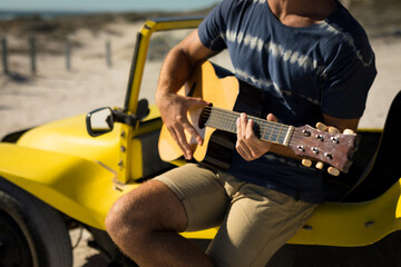 Midsection of caucasian man sitting on beach buggy playing guitar
