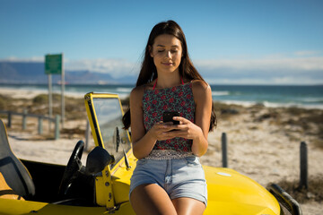 Fototapeta na wymiar Happy caucasian woman sitting on beach buggy by the sea using smartphone
