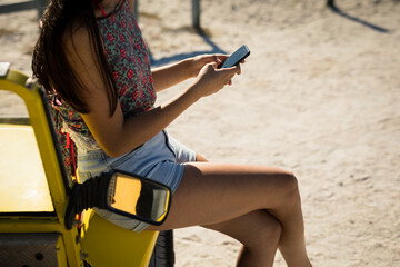 Midsection of caucasian woman sitting on beach buggy by the sea using smartphone