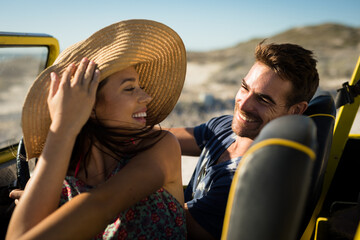 Happy caucasian couple sitting in beach buggy by the sea smiling