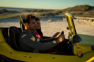 Happy caucasian couple sitting in beach buggy by the sea during sunset