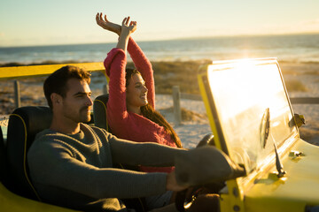 Happy caucasian couple sitting in beach buggy by the sea during sunset