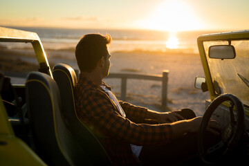 Caucasian man sitting in beach buggy by the sea during sunset