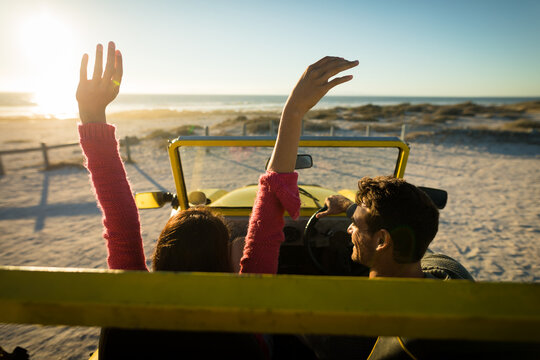 Happy caucasian couple sitting in beach buggy by the sea during sunset