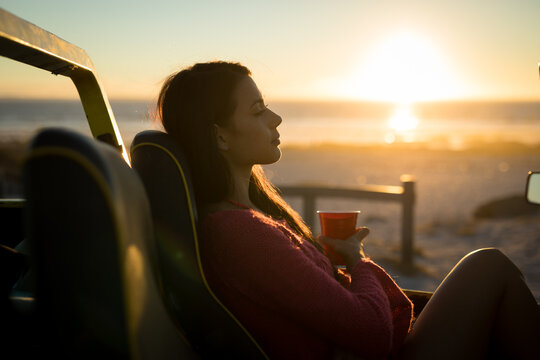 Caucasian woman sitting in beach buggy by the sea during sunset relaxing