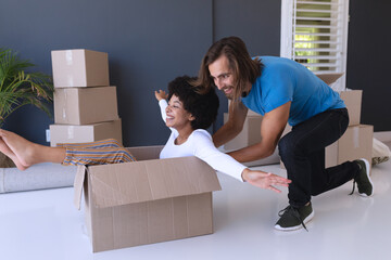 Happy diverse couple moving house smiling and playing with cartons