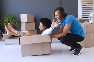 Happy diverse couple moving house smiling and playing with cartons