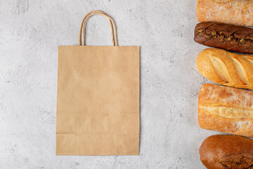Baking background with eco disposable paper bag from a supermarket recyclable and whole fresh baked loaves of bread top view on gray background with mockup