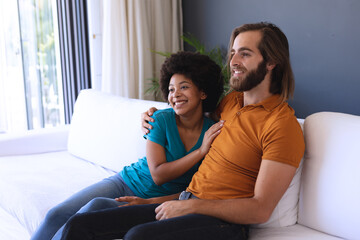 Obraz premium Happy diverse couple sitting on sofa embracing and smiling