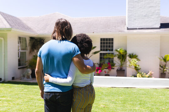 Diverse Couple Embracing In Front Of House On Sunny Garden Terrace