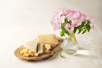 Different types of cheeses on a wooden board. A bouquet of delicate pink flowers.. Symbols of Jewish holiday - Shavuot