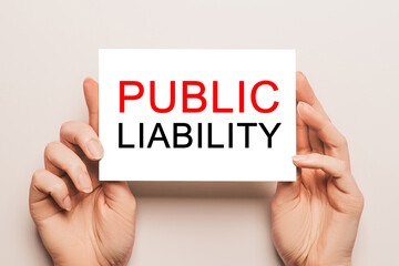 Female hands hold card paper with text PUBLIC LIABILITY on a yellow background. Business and finance concept