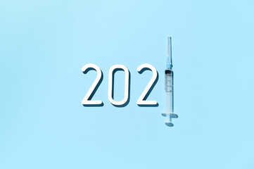 The 2021 - year of mass vaccination against COVID-19 of world population, the concept of victory over coronavirus. Overhead view of date 2021, syringe on pastel blue background