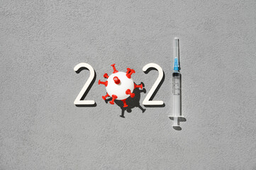 The 2021 - year of mass vaccination against COVID-19 of world population, the concept of victory over coronavirus. Overhead view of number 2021, syringe, and ball in form virus on gray background