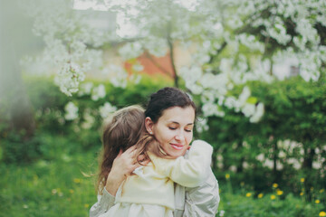 Happy mother's day. Little girl hugs her mother in the spring cherry garden. Portrait of happy mother and daughter among white flowers trees. Family values. Motherhood. Mom and child in blooming park.