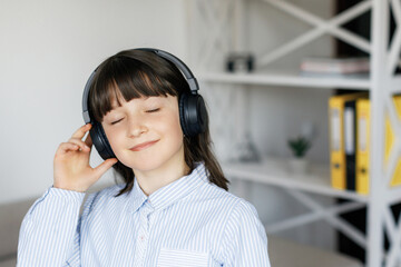 Happy funny teen girl with dark hair wear headphones standing in room and listening new pop music, enjoying, singing song, relaxing in cozy living room at home.