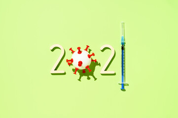 2021 - year of mass vaccination against COVID-19 of world population, the concept of victory over coronavirus. Overhead view of number 2021, syringe, and ball in form virus on pastel green background