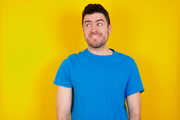 Obraz premium Amazed young handsome caucasian man wearing blue t-shirt against yellow background bitting lip and looking tricky to empty space.