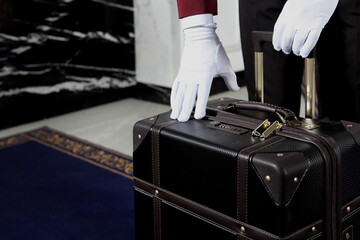 Doorman is holding a suitcase. Unrecognizable photo. Only white-gloved hands. Hotel service. Hotel...
