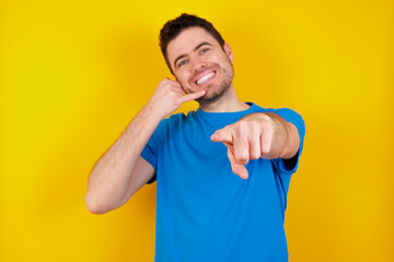 young handsome caucasian man wearing blue t-shirt against yellow background smiling cheerfully and...