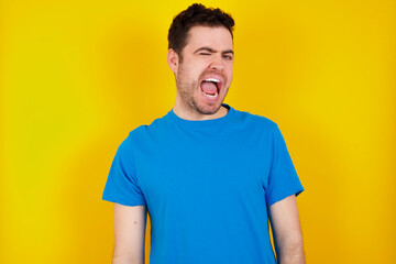 Fototapeta premium young handsome caucasian man wearing blue t-shirt against yellow background winking looking at the camera with sexy expression, cheerful and happy face.