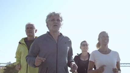 Active pensioners jogging outside. Group of elderly people in sporty clothes keeping fit, running down street together. Front view. Elderly age and lifestyle concept