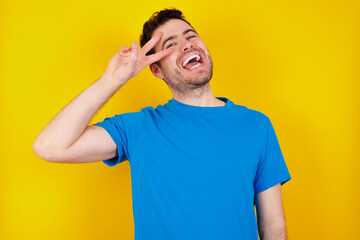Cheerful cheery optimistic young handsome caucasian man wearing blue t-shirt against yellow background holding two palms copy space