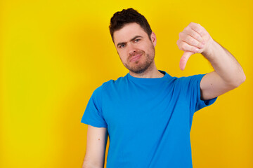 young handsome caucasian man wearing blue t-shirt against yellow background making fun of people with fingers on forehead doing loser gesture mocking and insulting.