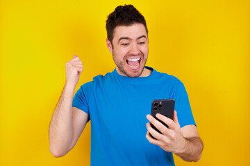 young handsome caucasian man wearing blue t-shirt against yellow background using mobile phone...