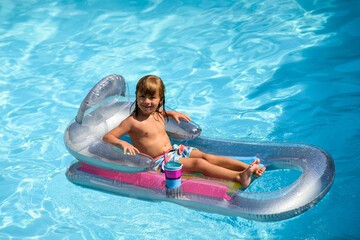 Summertime vacation. Child in pool. Boy swimming at swimmingpool. Funny kid on inflatable rubber mattress.