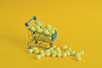Shopping trolley with yellow easter eggs on yellow background. Easter sale.