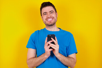 young handsome caucasian man wearing blue t-shirt against yellow background Mock up copy space. Using mobile phone, typing sms message