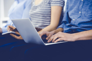 Naklejka premium Group of casual dressed business people working at meeting or conference, close-up of hands. Businessman using laptop computer. Teamwork or coaching concept