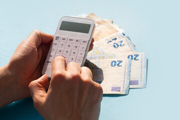 a white calculator in a woman's hand and euro banknotes on a blue background