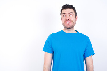 Fototapeta premium Amazed young handsome caucasian man wearing blue t-shirt against white background bitting lip and looking tricky to empty space.