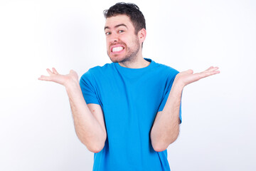 Clueless young handsome caucasian man wearing blue t-shirt against white background shrugs...
