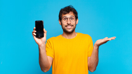 young handsome indian man doubting or uncertain expression and holding a mobile telephone