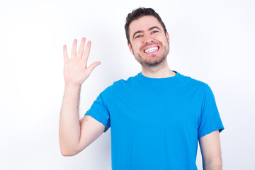 young handsome caucasian man wearing blue t-shirt against white background Waiving saying hello happy and smiling, friendly welcome gesture.