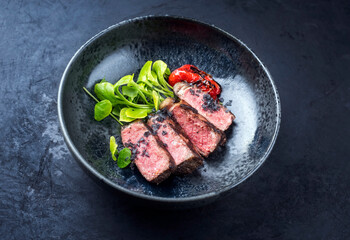 Modern style traditional dry aged sliced wagyu roast beef with fried onion rings served as top view on a rustic black board