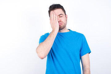 Tired overworked young handsome caucasian man wearing blue t-shirt against white has sleepy...
