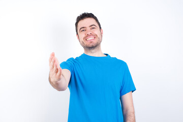 young handsome caucasian man wearing blue t-shirt against white background smiling friendly offering handshake as greeting and welcoming. Successful business.