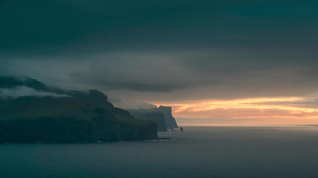 Time lapse of sunset at the north coast of Eysturoy with cliff layers and rock formation Risin og Kellingin and dark clouds over the ocean, Kalsoy Faroe Islands
