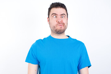 Fototapeta premium young handsome caucasian man wearing blue t-shirt against white background making grimace and crazy face, screaming out of control, funny lunatic expressing freedom and wild.