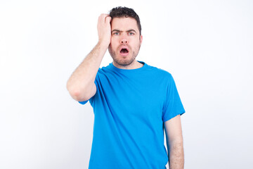 Obraz premium Embarrassed young handsome caucasian man wearing blue t-shirt against white background with shocked expression, expresses great amazement, Puzzled model poses indoor