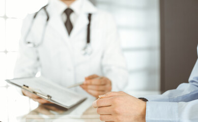 Unknown male doctor and woman-patient discussing current health examination while sitting in clinic...