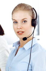 Blond woman call operator is using computer and headset for consulting clients online. Group of diverse people working as customer service occupation. Business concept