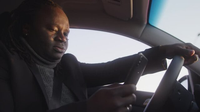 Young african american black man using smartphone and sending messages while driving. High quality 4k footage
