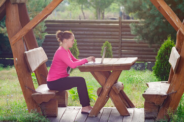 Young girl working on a laptop in a wooden gazebo in nature