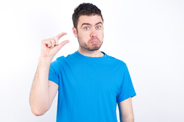 young handsome caucasian man wearing white t-shirt against white background purses lip and gestures with hand, shows something very little.