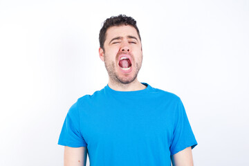 young handsome caucasian man wearing white t-shirt against white background yawns with opened mouth stands. Daily morning routine